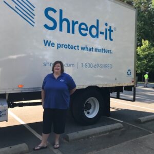 A woman smiles beside a truck reading Shred-it