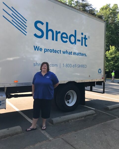 A woman smiles beside a truck reading Shred-it
