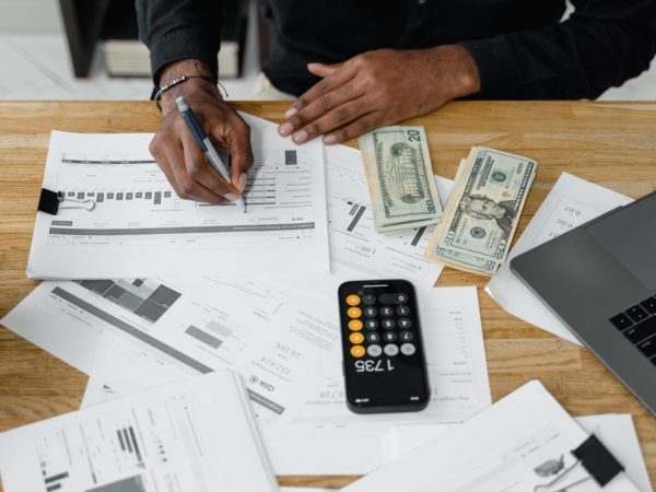 Papers and a calculator are scattered on a table, a person is filling out documentation