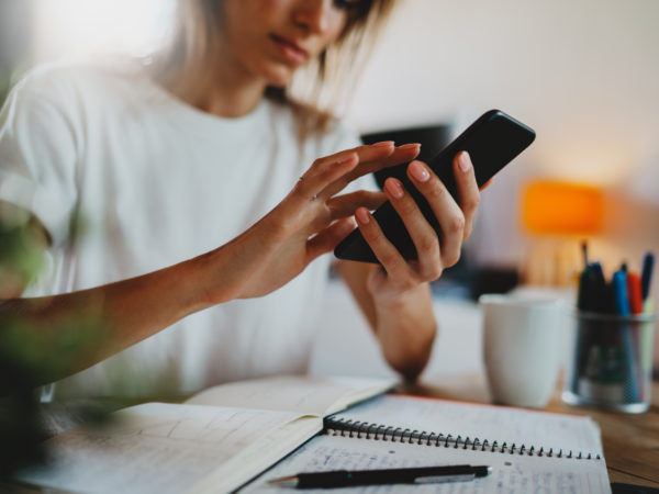 A woman typing on a phone seriously as she looks at an open notebook