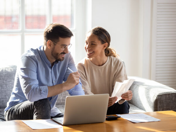 A young couple talking about papers over an open laptop