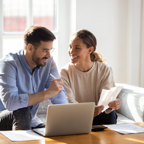 A young couple talking about papers over an open laptop