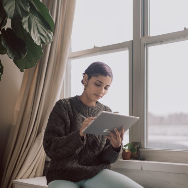 A woman working on her tablet by a window