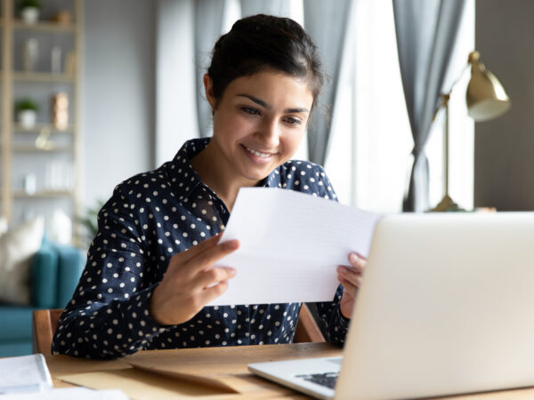 Smiling woman holding reading paper letter sit at table