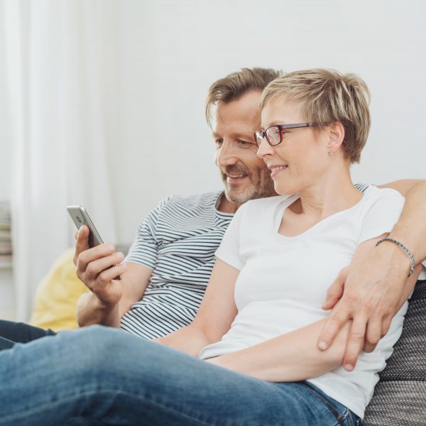 a couple sitting on the couch looking at a phone