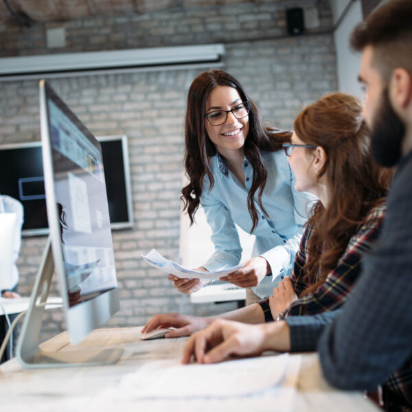 Women holding papers talking to a coworker at a computer