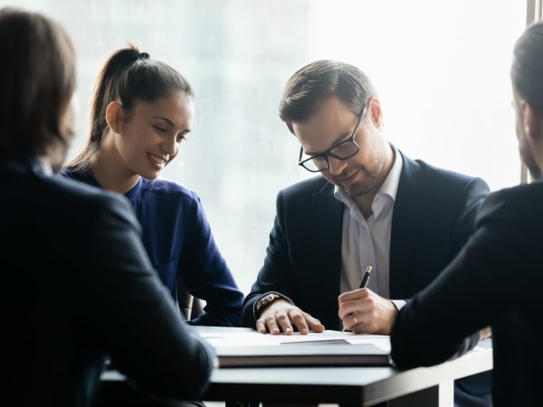 view of man signing paper with 3 other individuals watching