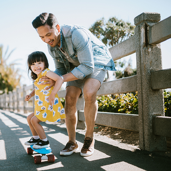 A dad helps his little girl go skateboarding, holding her waist for support