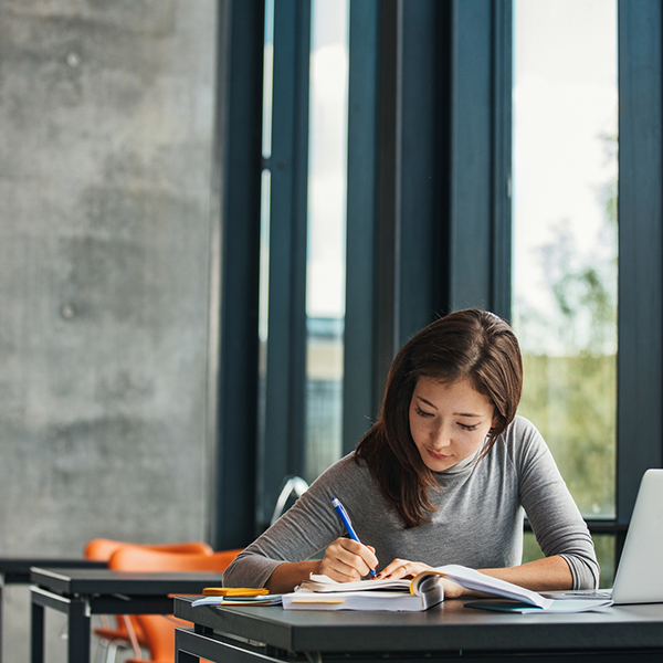 Young Asian female student sitting at table and writing on notebook. Young female student studying in library.