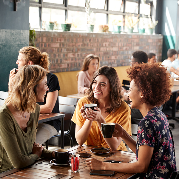 Three Young Female Friends Meeting Sit At Table In Coffee Shop A