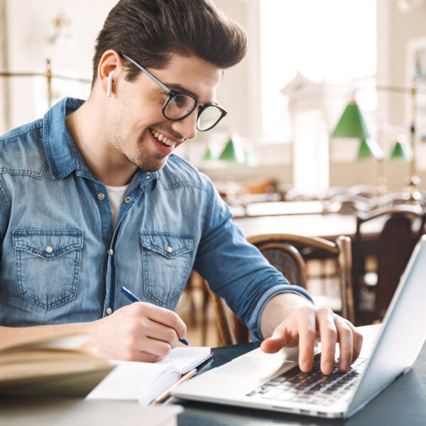 Smiling male student studying at the library, using laptop computer