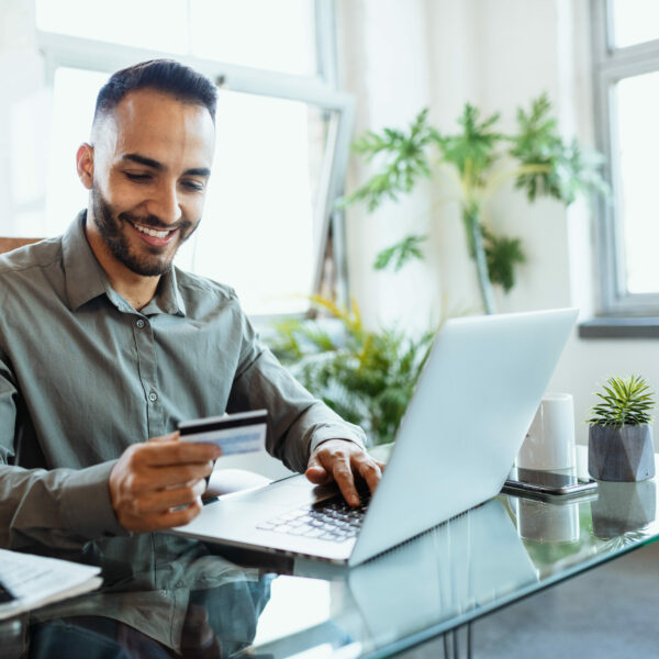 Man sitting at computer holding debit card, shopping online.