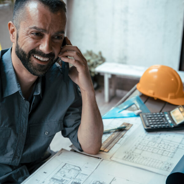 Male architect talking on a mobile phone with blueprints on desk.