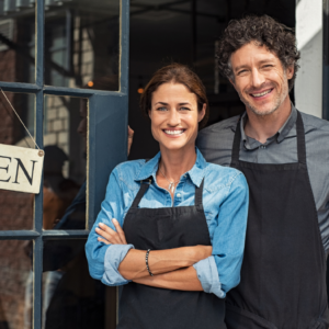 Male and female business owners standing in front of open door with an open sign.