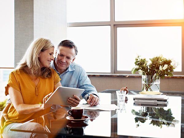 Mature couple sitting at their dining room table using a tablet