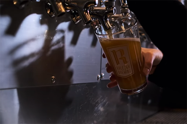 Person filling a glass with Raleigh Brewing logo etched on it.