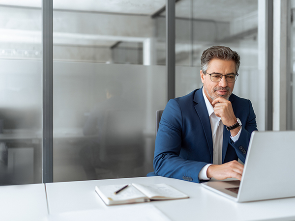 Focused businessman sitting at desk working laptop computer in office.