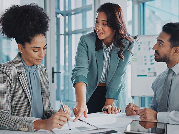 Group of business people at a table, with one individual highlighting a document as the others listen