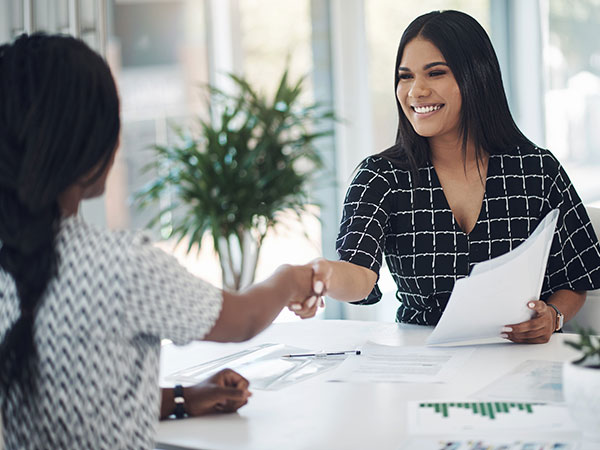 Two women in a business setting finalizing paperwork with a handshake