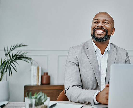 Businessman at his desk, looking up from his computer with a smile