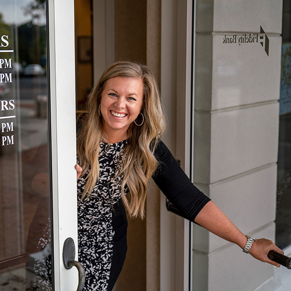 Friendly banker smiling while holding the door open. Welcome customer into the branch.